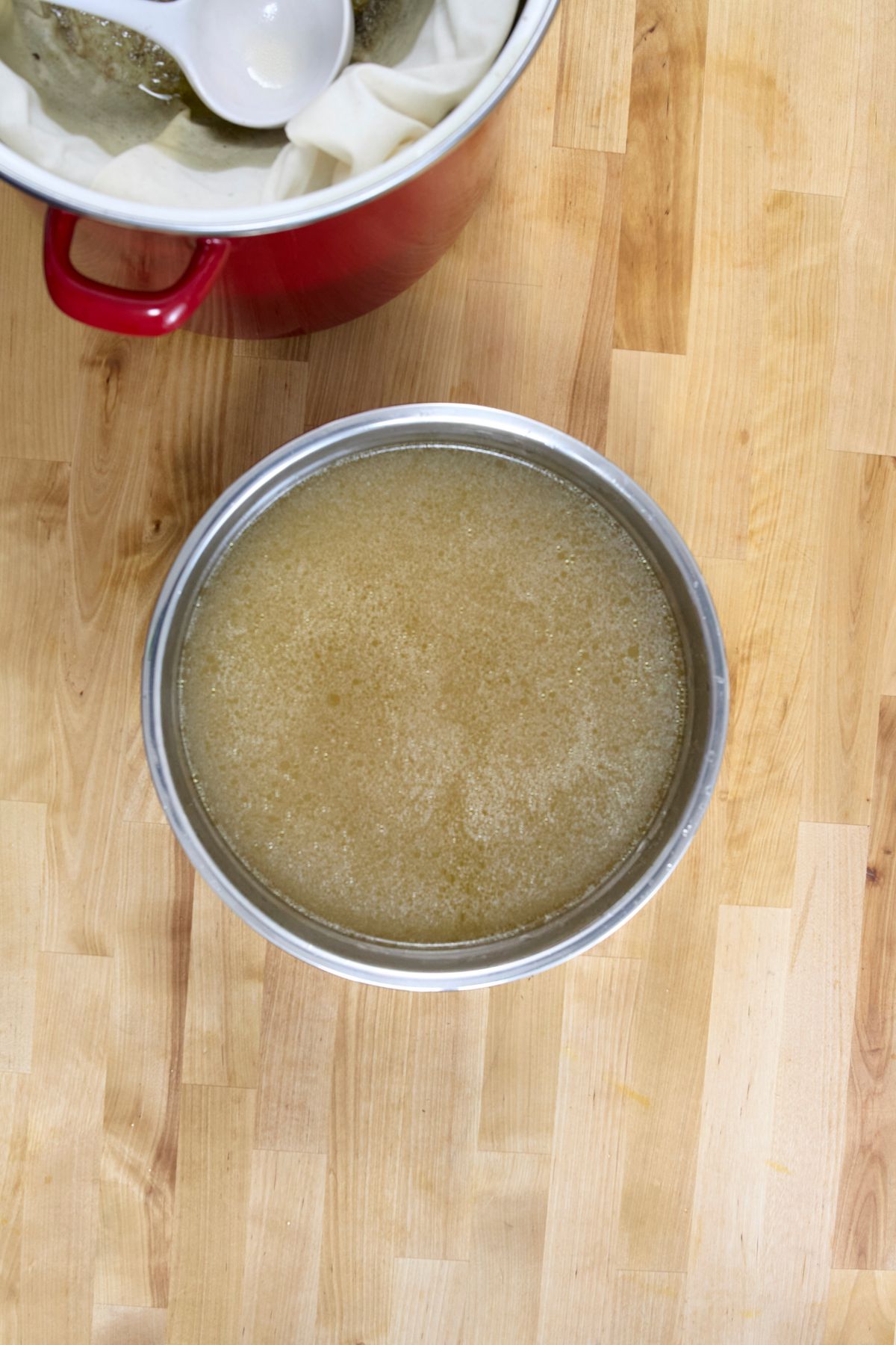Overhead view of a pot filled with strained chicken broth on a wooden countertop.