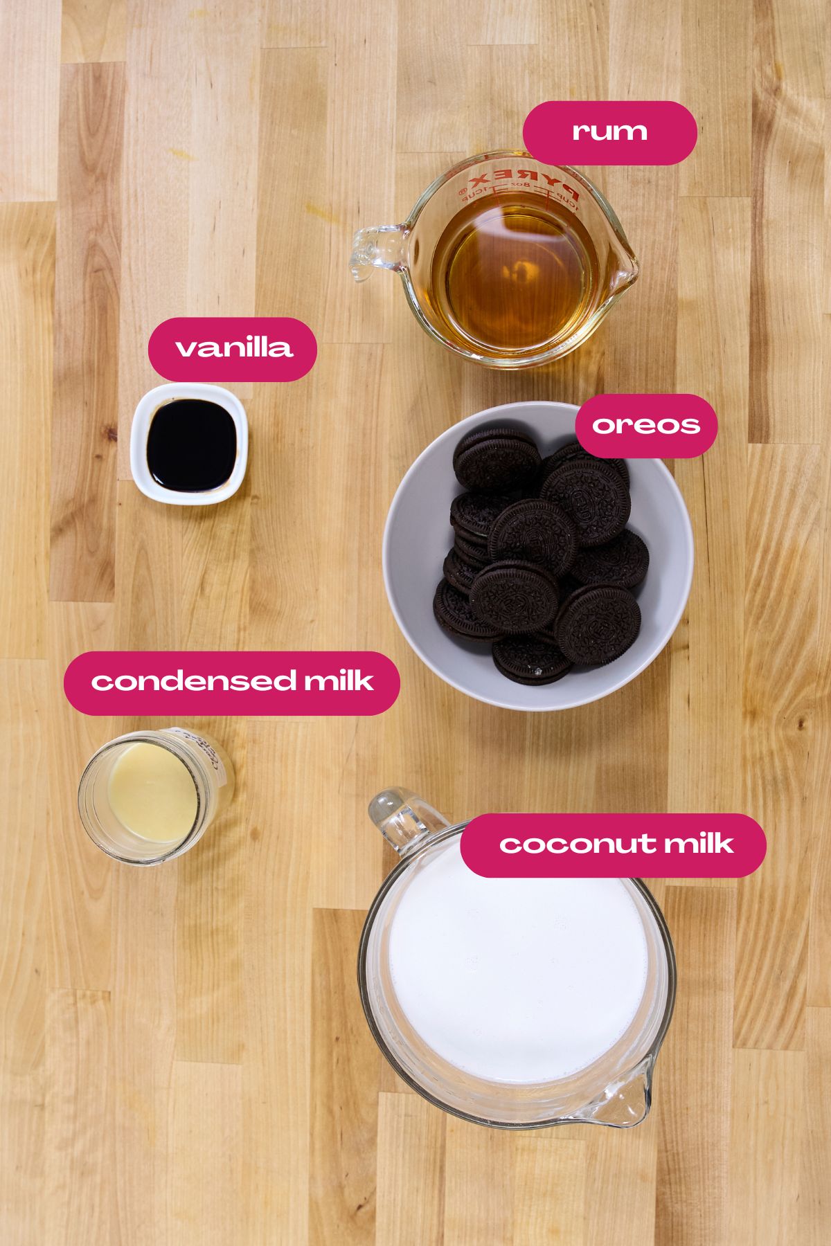 Flat lay of coquito ingredients: bowl of Oreo cookies, coconut milk, condensed milk, vanilla extract, and rum, each labeled with text.