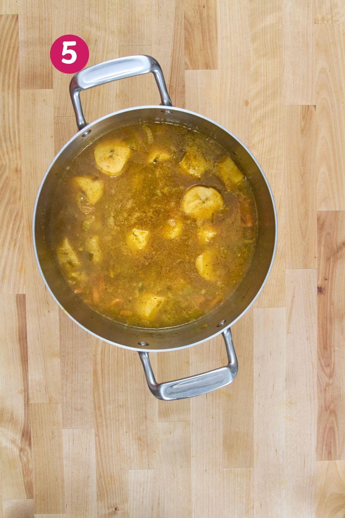 Pot with sliced plantains simmering in broth viewed from above on a wooden countertop.