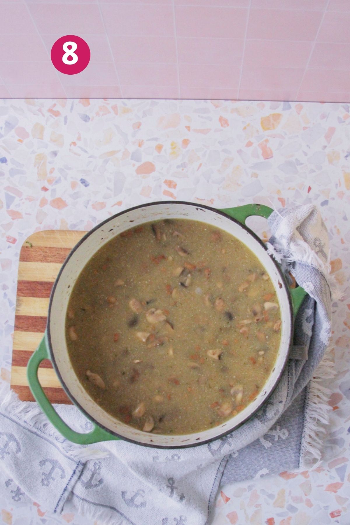 Overhead view of a green Dutch oven filled with blended bacon mushroom soup on a cutting board and folded kitchen towel, with a step number label in the corner.