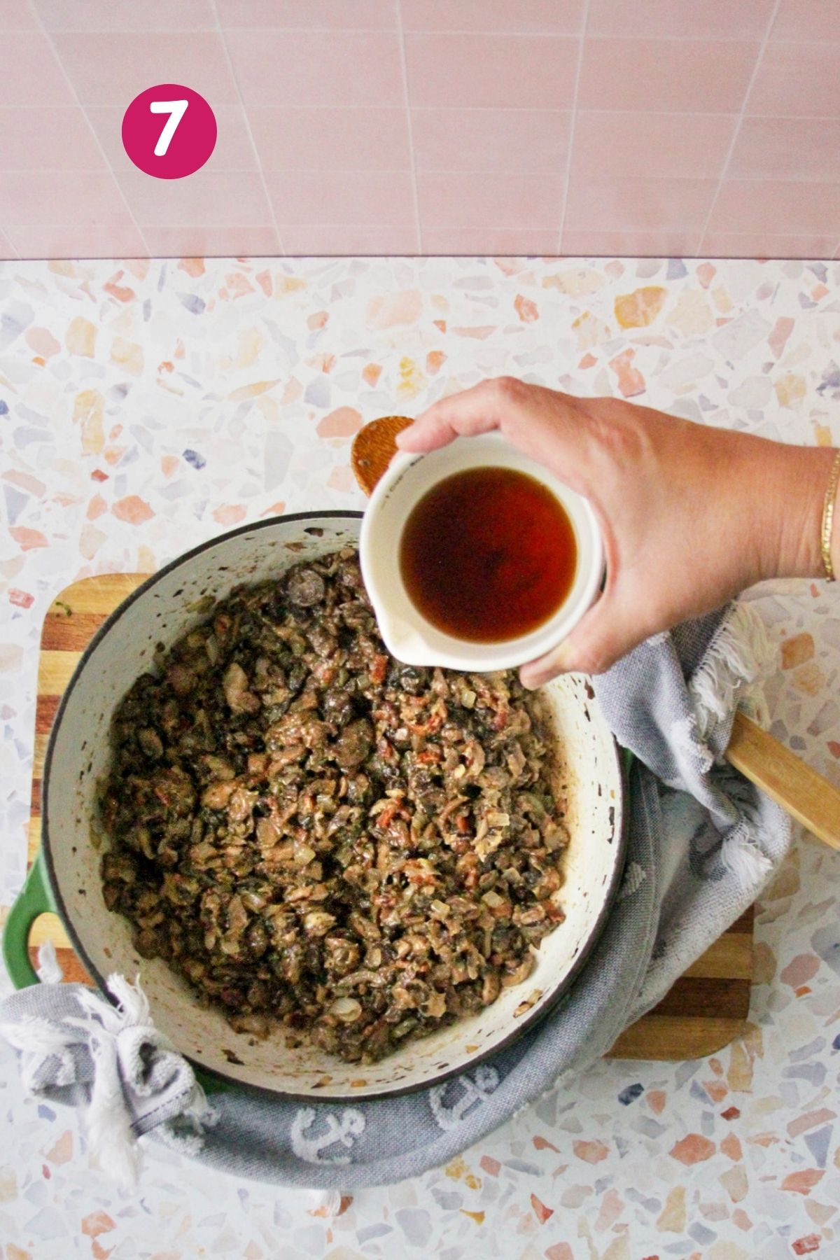 Hand pouring Marsala wine into a pot of cooked mushrooms and bacon to deglaze the pan, photographed from overhead.