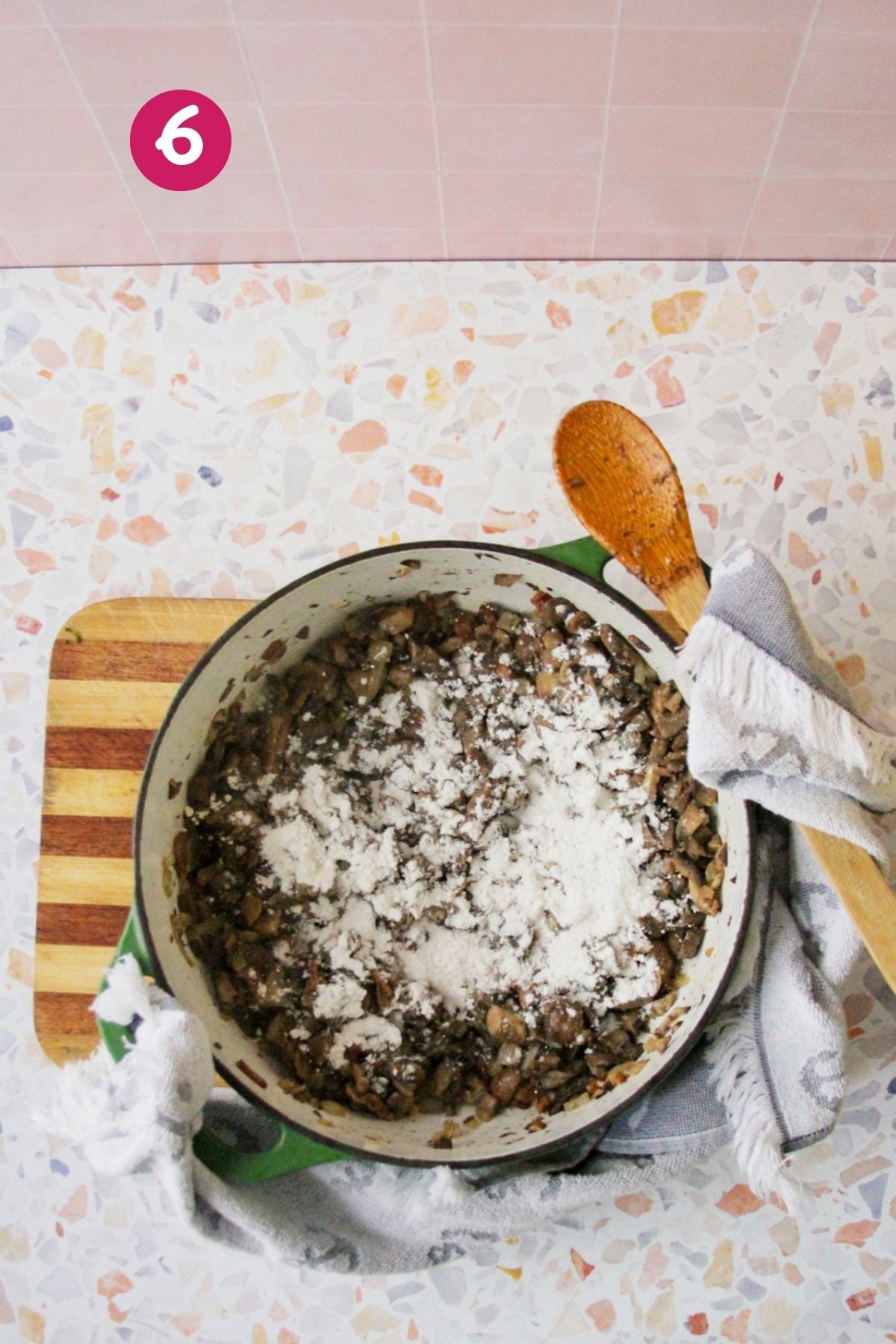 Flour sprinkled over cooked mushrooms and bacon in a Dutch oven to form a roux, photographed from overhead.