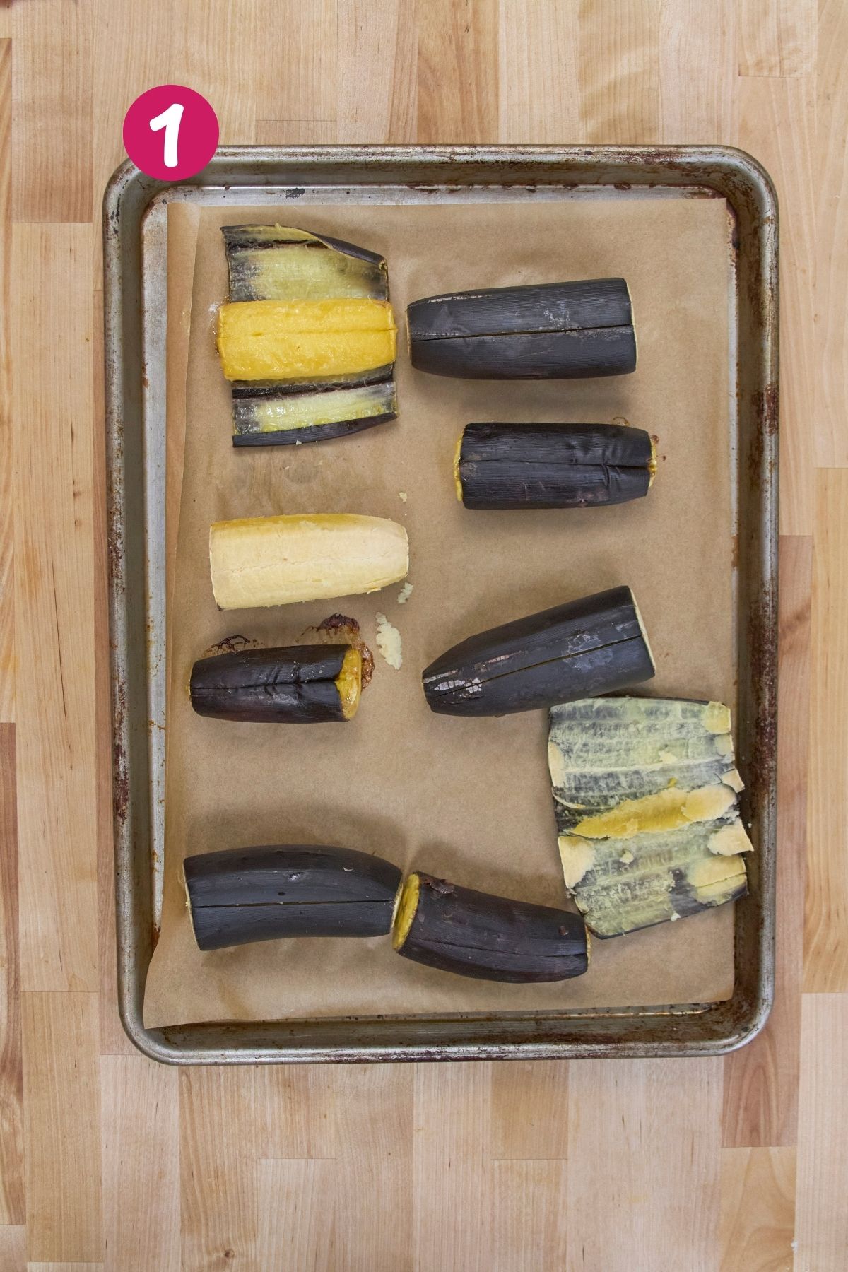 Roasted plantains on a parchment-lined baking sheet, some peeled and some with skins intact.