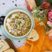 Overhead view of two bowls of white bean chicken chili served on green plates with bread slices on a cutting board, and flowers arranged on an orange cloth.