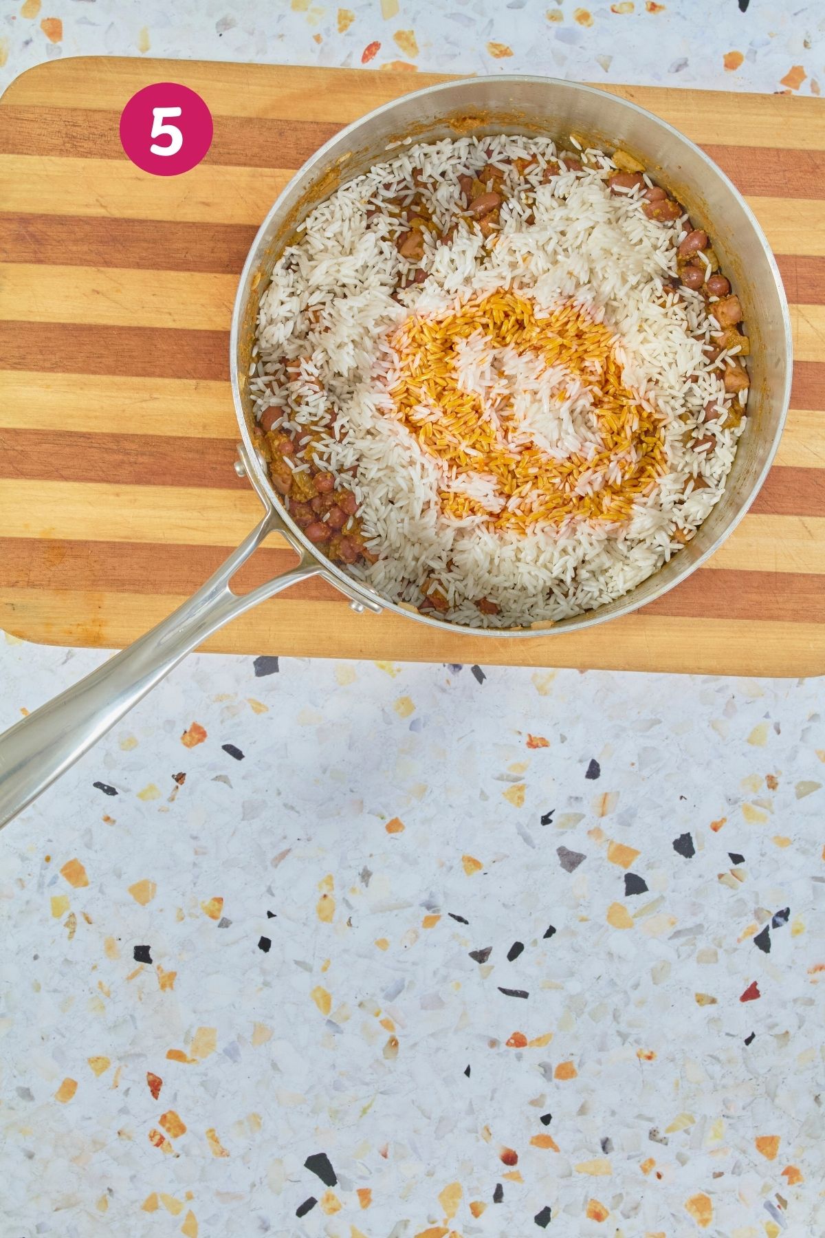 Overhead view of white rice and orange achiote oil added to bean mixture in stainless steel pot, labeled with step 5.