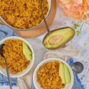 Overhead view of Puerto Rican arroz con habichuelas (rice and beans) in glass bowl and two white bowls with avocado slices and peach peonies.