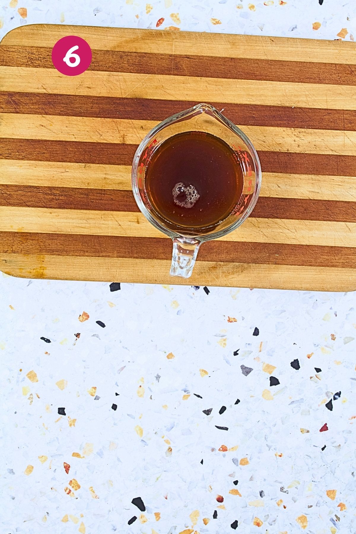 Glass measuring cup filled with amber-colored broth for cooking rice with beans on wooden cutting board, labeled with step 6.