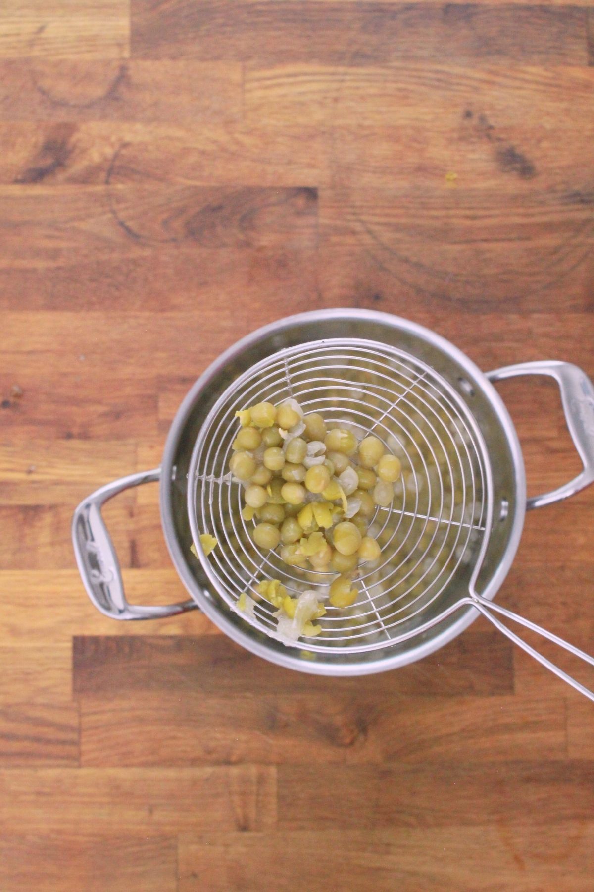 Overhead view of cooked gandules (pigeon peas) draining in wire mesh strainer set over a stainless steel pot.