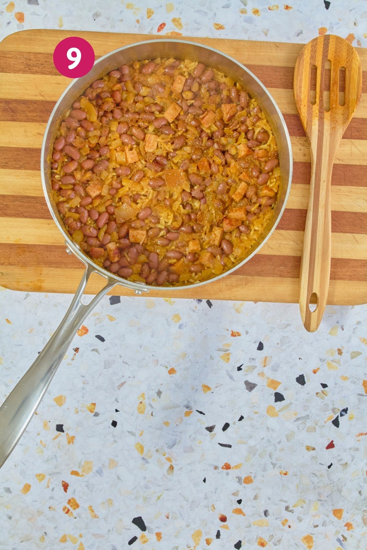 Overhead view of fully cooked arroz con habichuelas with fluffy separated rice grains and beans in a stainless steel pot, labeled with step 9.