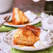 Slice of flancocho on vintage plate with caramel topping and whipped cream, additional serving blurred in background.