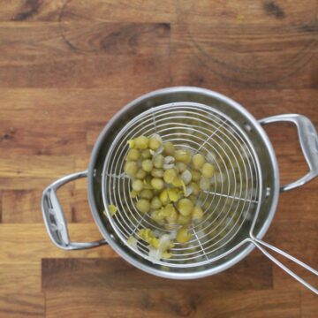 Cooked gandules (pigeon peas) with split skins draining in wire mesh strainer over a stainless steel pot.