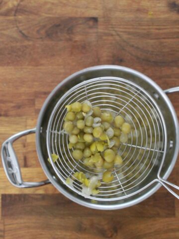Cooked gandules (pigeon peas) with split skins draining in wire mesh strainer over a stainless steel pot.