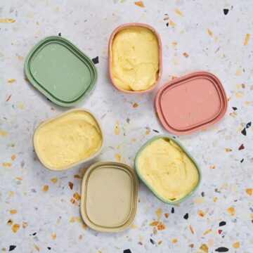 Overhead view of orange honey butter in pastel colored dishes arranged on a speckled surface.