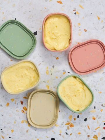 Overhead view of orange honey butter in pastel colored dishes arranged on a speckled surface.