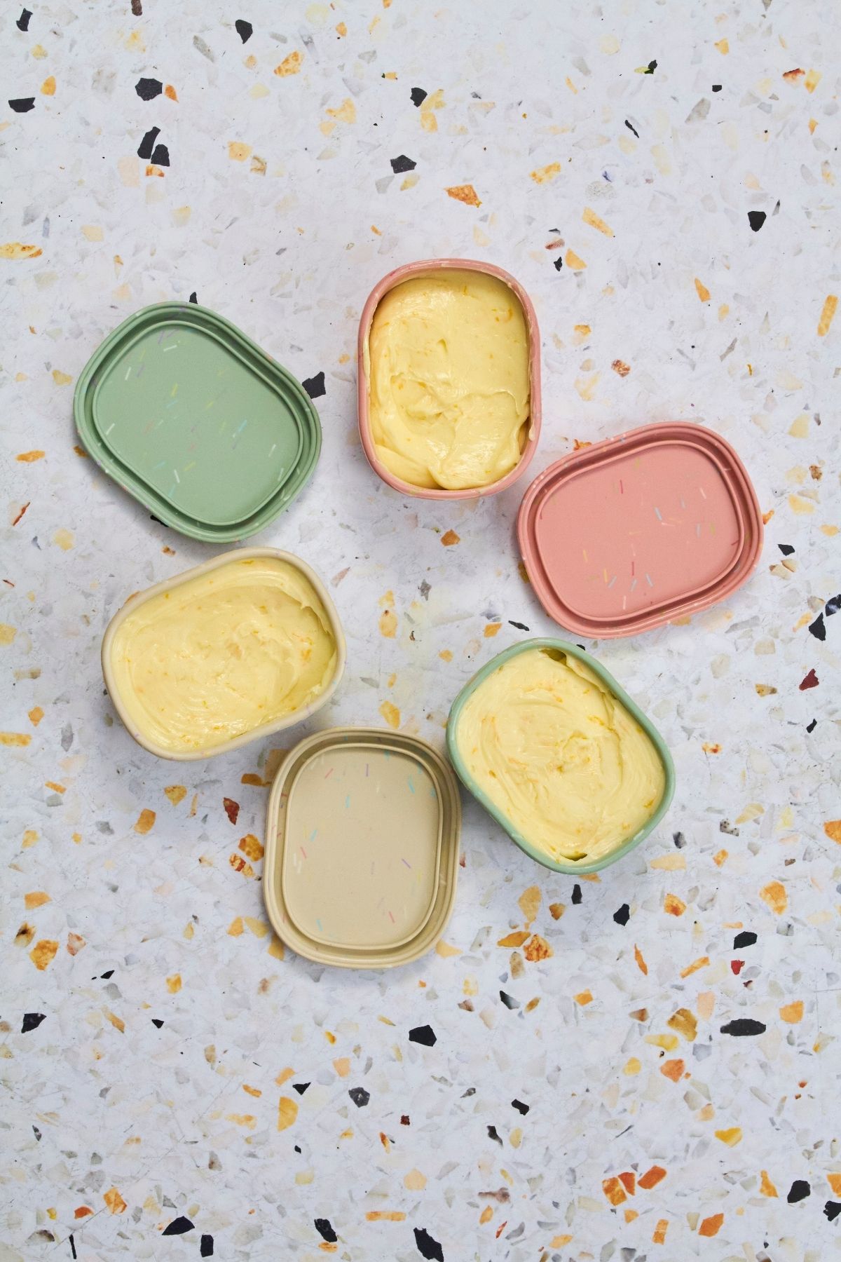 Homemade orange honey butter in pastel containers on terrazzo countertop.