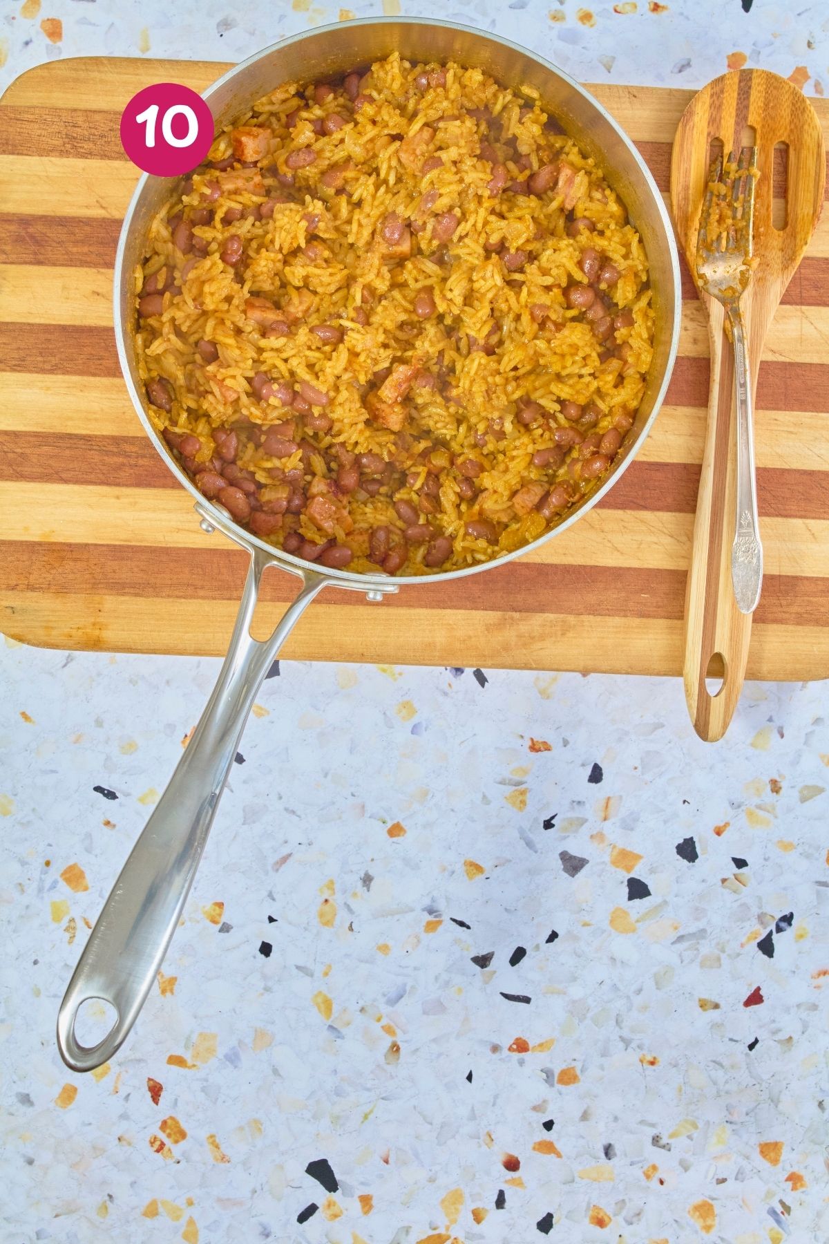 Overhead view of fully cooked arroz con habichuelas with fluffy separated rice grains and beans in a stainless steel pot, labeled with step 10.
