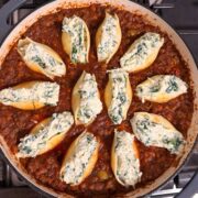 Close-up overhead view of stuffed pasta shells filled with a ricotta and spinach mixture, arranged in a rich red meat sauce in a large skillet.