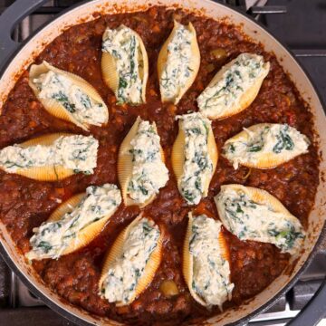 Close-up overhead view of stuffed pasta shells filled with a ricotta and spinach mixture, arranged in a rich red meat sauce in a large skillet.