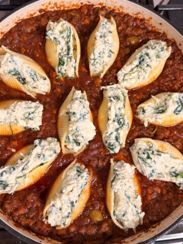 Close-up overhead view of stuffed pasta shells filled with a ricotta and spinach mixture, arranged in a rich red meat sauce in a large skillet.