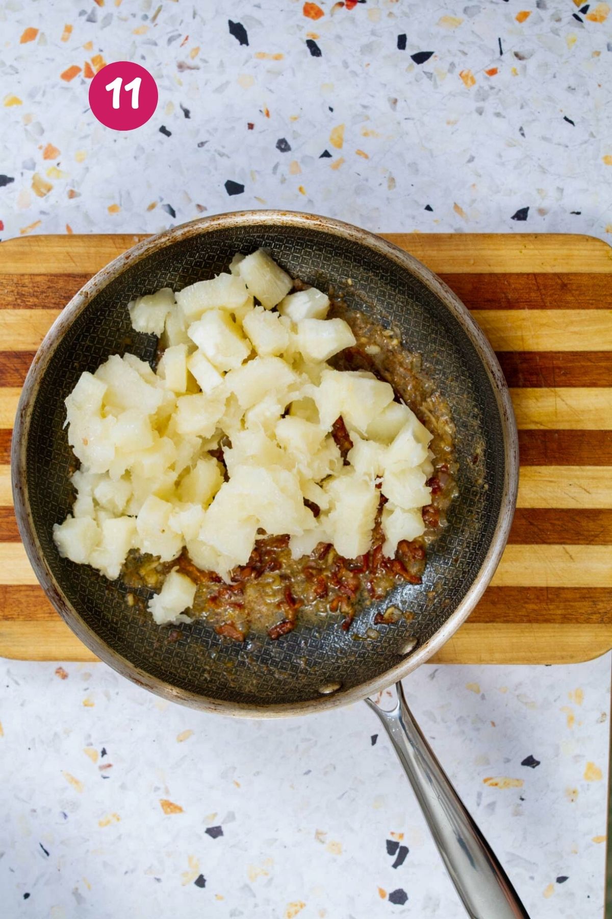 Adding cubed boiled yuca to a nonstick skillet with bacon vinaigrette and sofrito.
