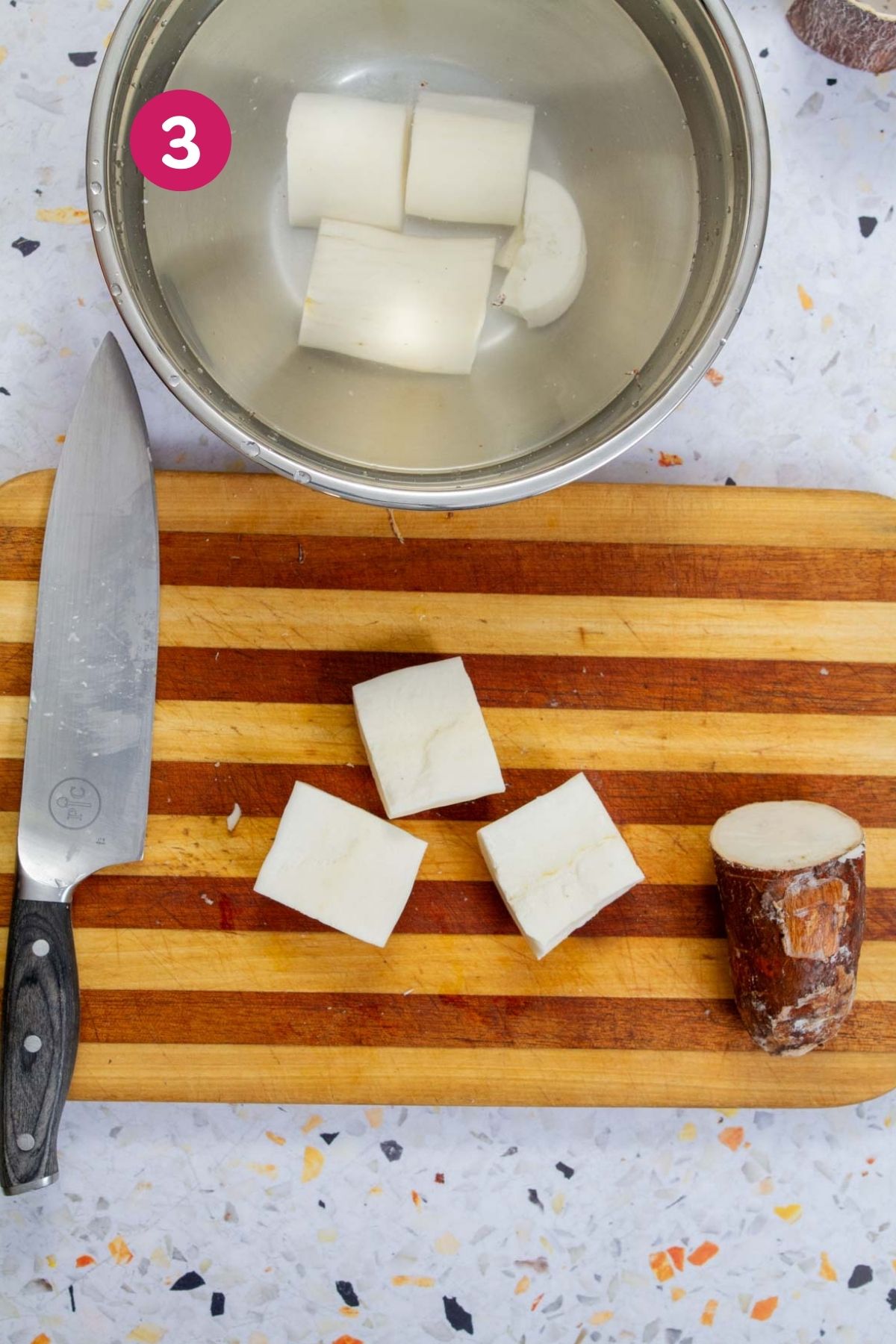 Peeled yuca root cut into large chunks on a striped wooden cutting board, ready for boiling.