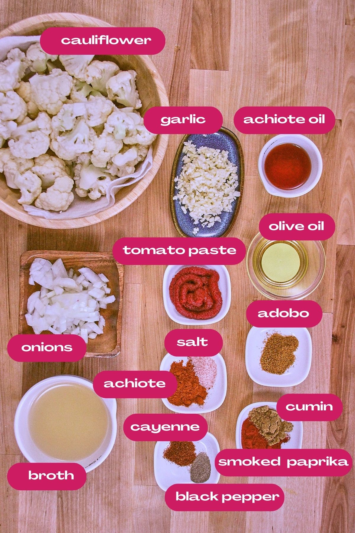 Overhead view of cauliflower bravas ingredients, including cauliflower florets, onions, tomato paste, garlic, olive oil, achiote oil, adobo, salt, achiote, cumin, smoked paprika, black pepper, cayenne, and broth.