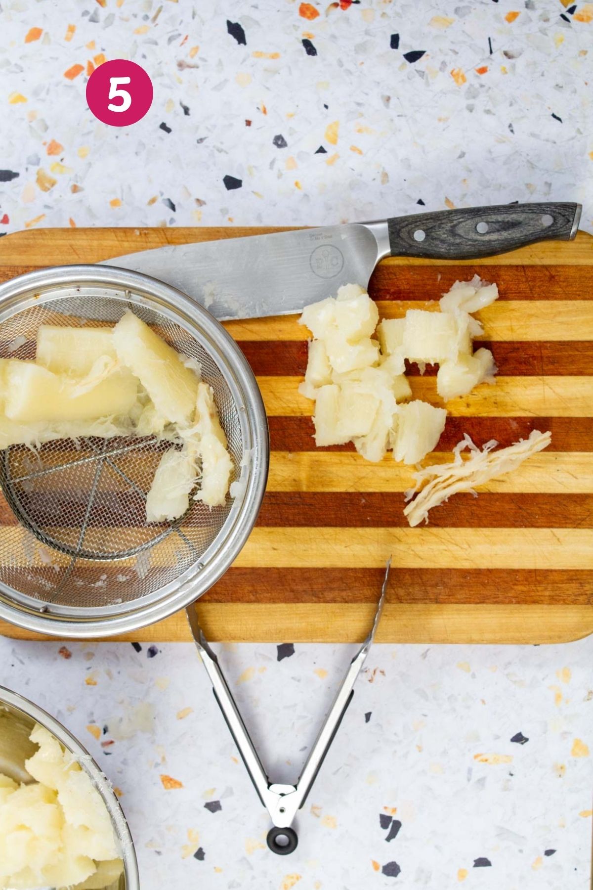 Dicing boiled yuca into bite-sized pieces on a striped wooden cutting board with a chef's knife and strainer.