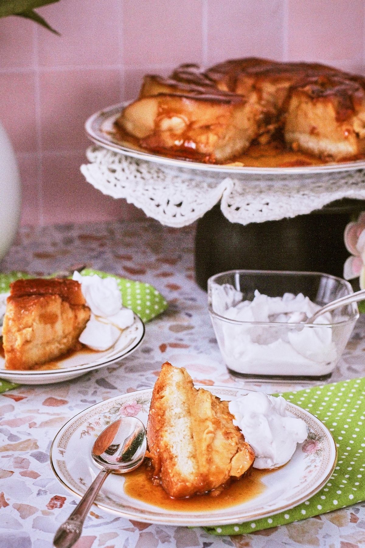 Two slices of flancocho on floral dessert plates with whipped cream, styled on a terrazzo surface with green polka dot napkins.