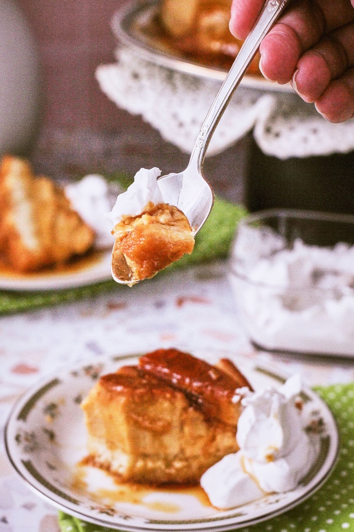 A spoonful of flancocho held up, showing the layered flan-and-cake texture, with a plated slice and whipped cream in the background.