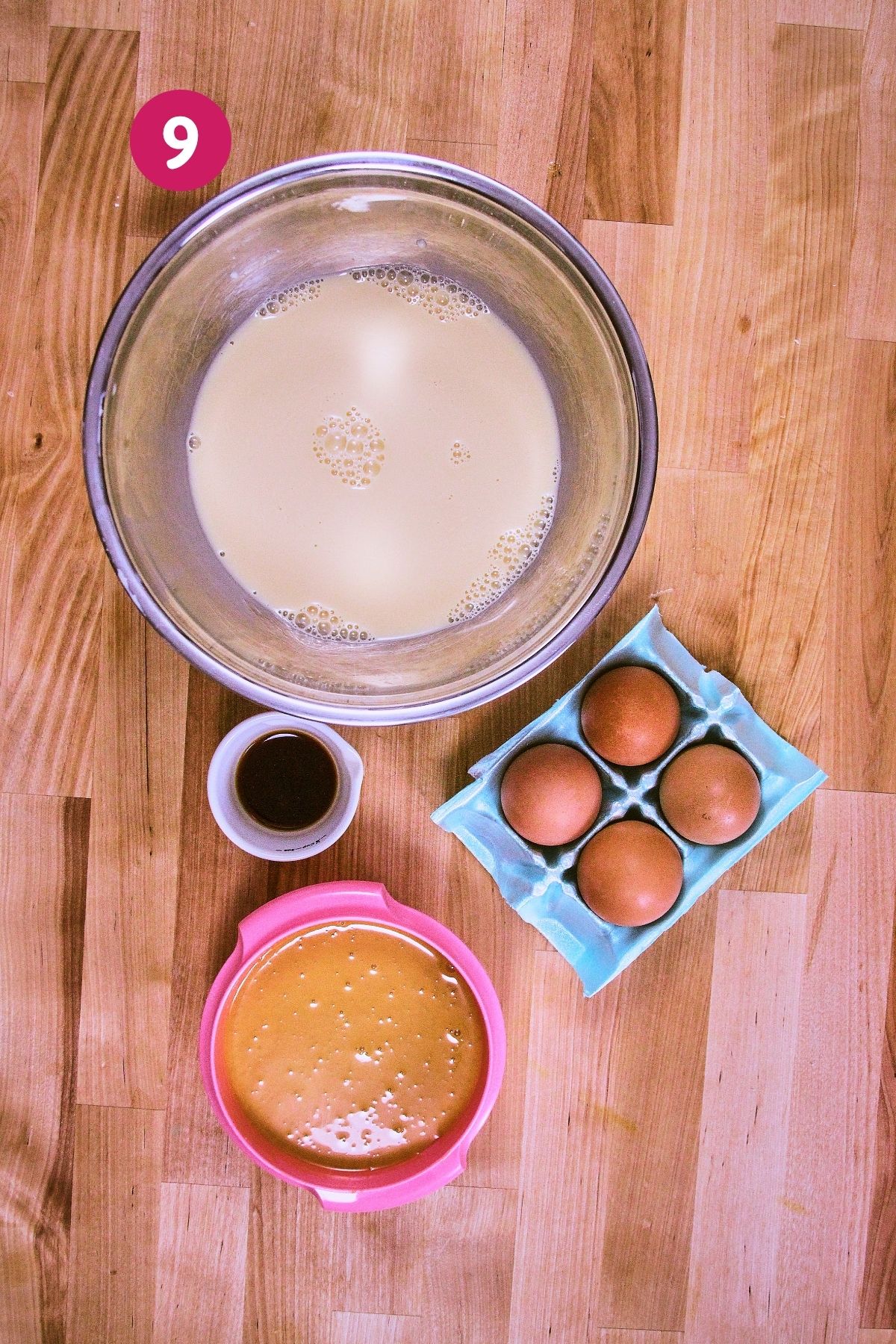 Flan custard ingredients laid out on a butcher block, including evaporated and condensed milks, eggs, and vanilla.