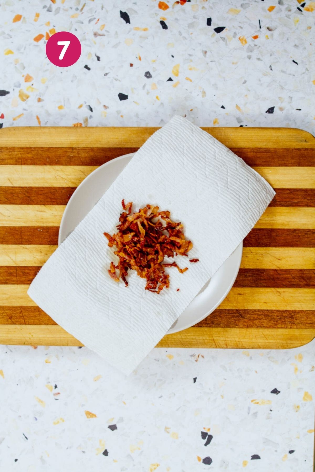 Crispy rendered bacon pieces are draining on a paper towel on a white plate next to a strainer with boiled yuca.