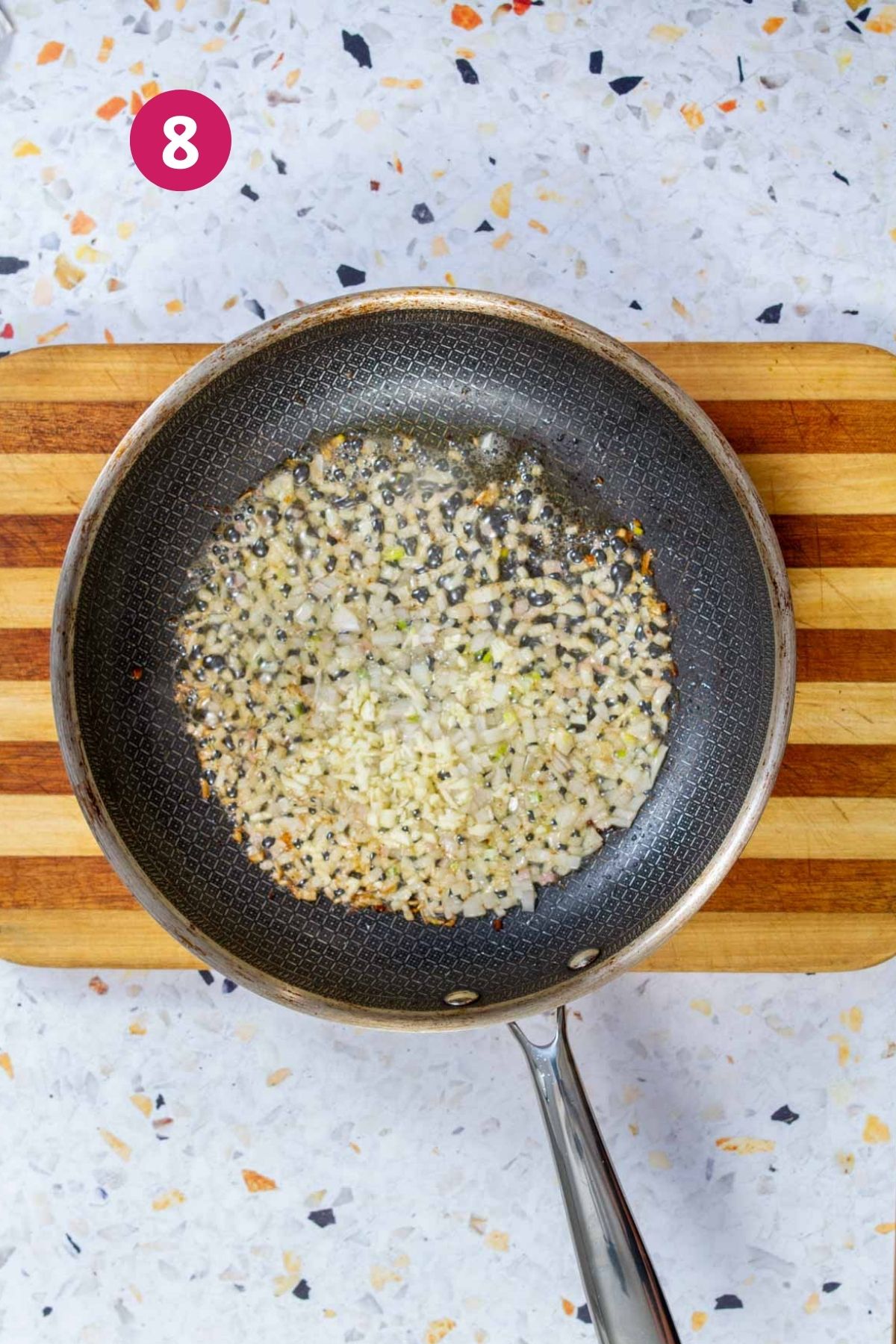 Diced shallots sautéing in bacon fat in a nonstick skillet until translucent.