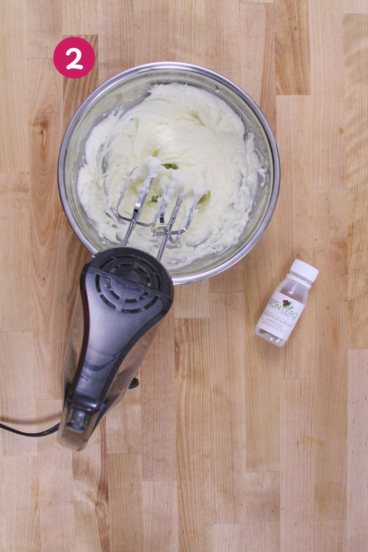 Creamed butter and coconut oil in a mixing bowl with a hand mixer, and a small bottle of almond extract ready to be added.