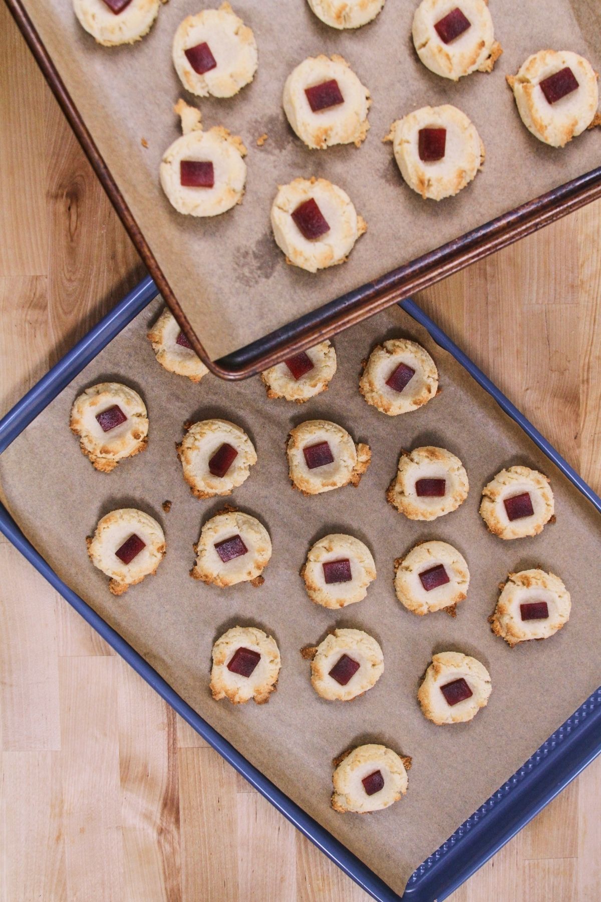 Overhead view of two baking sheets of freshly baked low-carb polvorones topped with guava paste, golden brown around the edges.