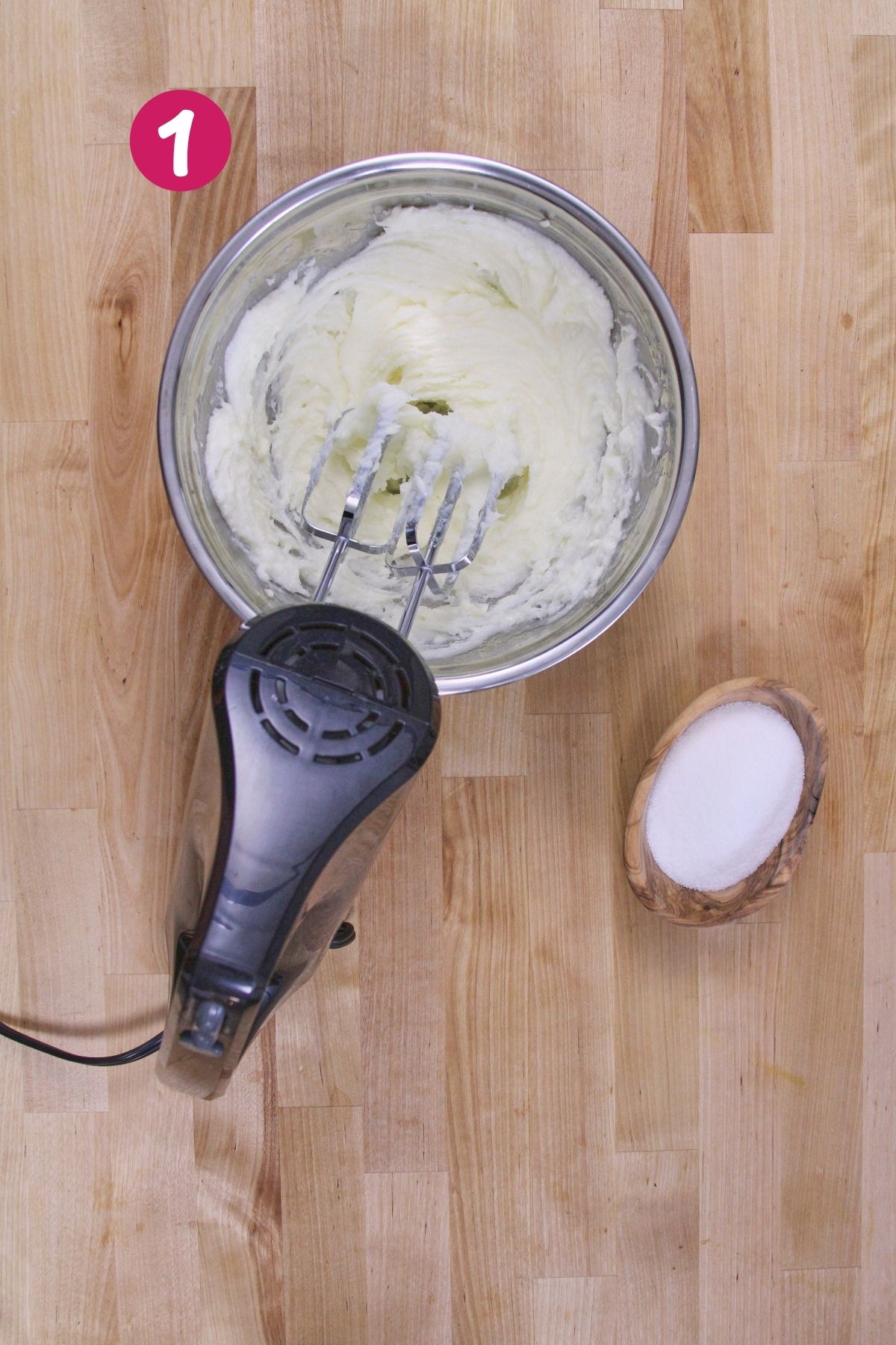 Creamed butter and coconut oil in a stainless steel mixing bowl with a hand mixer beside a small bowl of monk fruit sweetener.