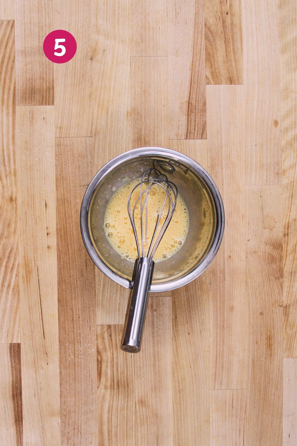 A lightly beaten egg in a small stainless steel bowl with a whisk.