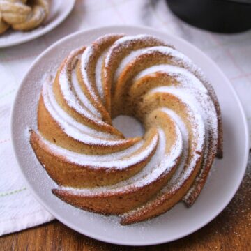 Puerto Rican spice cake hojaldre añasqueño displayed as a spiral bundt and mini bundts dusted with powdered sugar, surrounded by flowers and a lace doily.