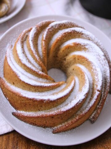 Puerto Rican spice cake hojaldre añasqueño displayed as a spiral bundt and mini bundts dusted with powdered sugar, surrounded by flowers and a lace doily.