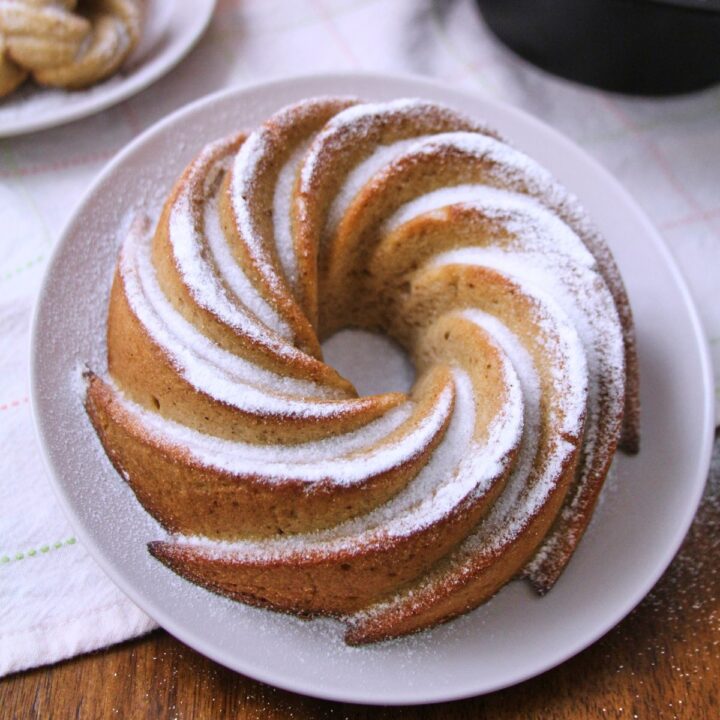Puerto Rican spice cake hojaldre añasqueño displayed as a spiral bundt and mini bundts dusted with powdered sugar, surrounded by flowers and a lace doily.