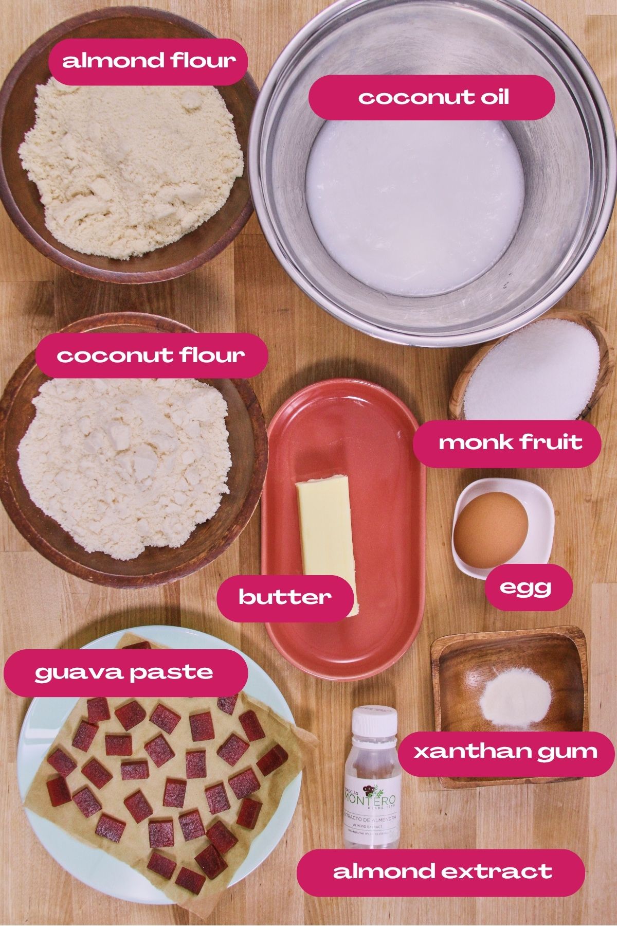 Flat lay of ingredients for low-carb polvorones, including almond flour, coconut flour, coconut oil, butter, monk fruit sweetener, egg, xanthan gum, almond extract, and guava paste on a wooden surface.