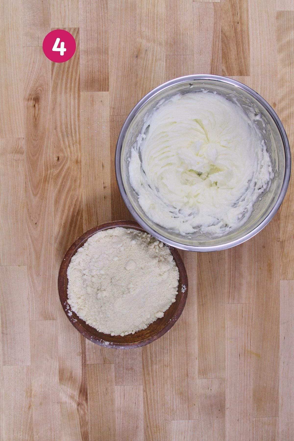 Creamed fat mixture in a stainless steel bowl beside a wooden bowl of combined alternative flours ready to mix.