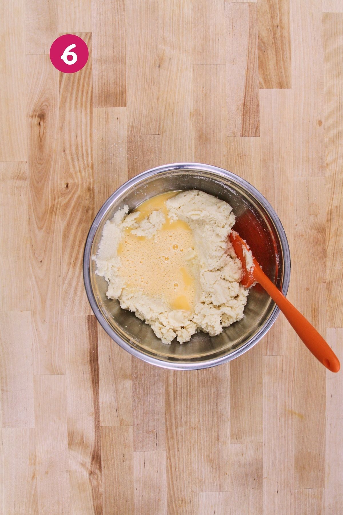 Beaten egg being folded into low-carb polvorón dough with an orange silicone spatula.