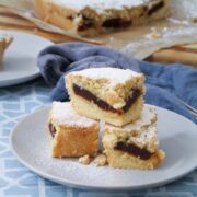 Three stacked panetela de guayaba bars on a gray plate showing the guava paste layer, with a blue linen and striped wood cutting board in the background.