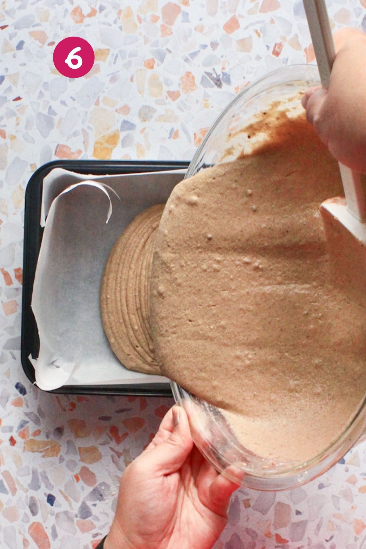 Hands pouring hojaldre añasqueño spiced cake batter into a parchment-lined square baking pan.