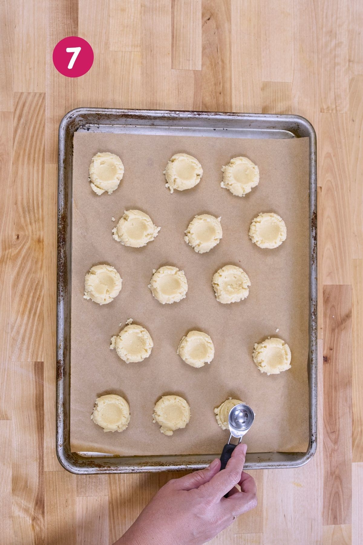 Low-carb polvorón dough scooped into uniform rounds on a parchment-lined baking sheet with a cookie scoop visible in hand.