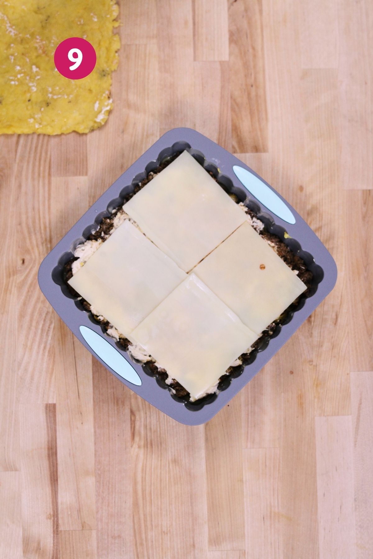 (Step 9) Four slices of Swiss cheese laid over the filling in the baking pan, with the mashed plantain top layer visible in the corner.