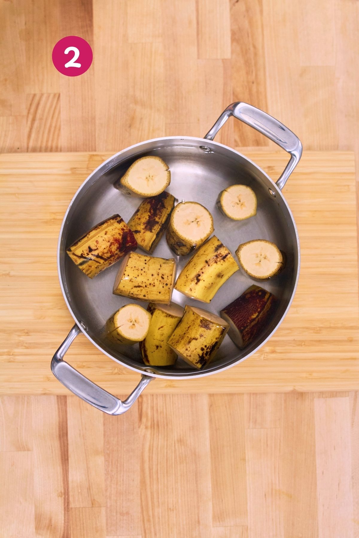 (Step 2) Ripe plantain chunks with skins still on, boiling in a stainless steel pot of water.