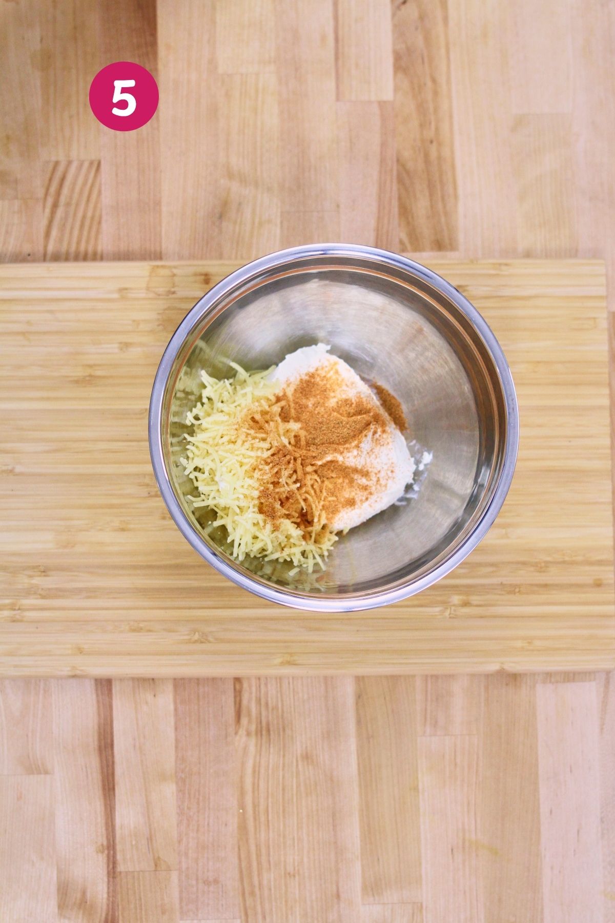(Step 5) Shredded cheese, cream cheese, and adobo seasoning in a stainless steel mixing bowl before combining for the pastelón cheese layer.