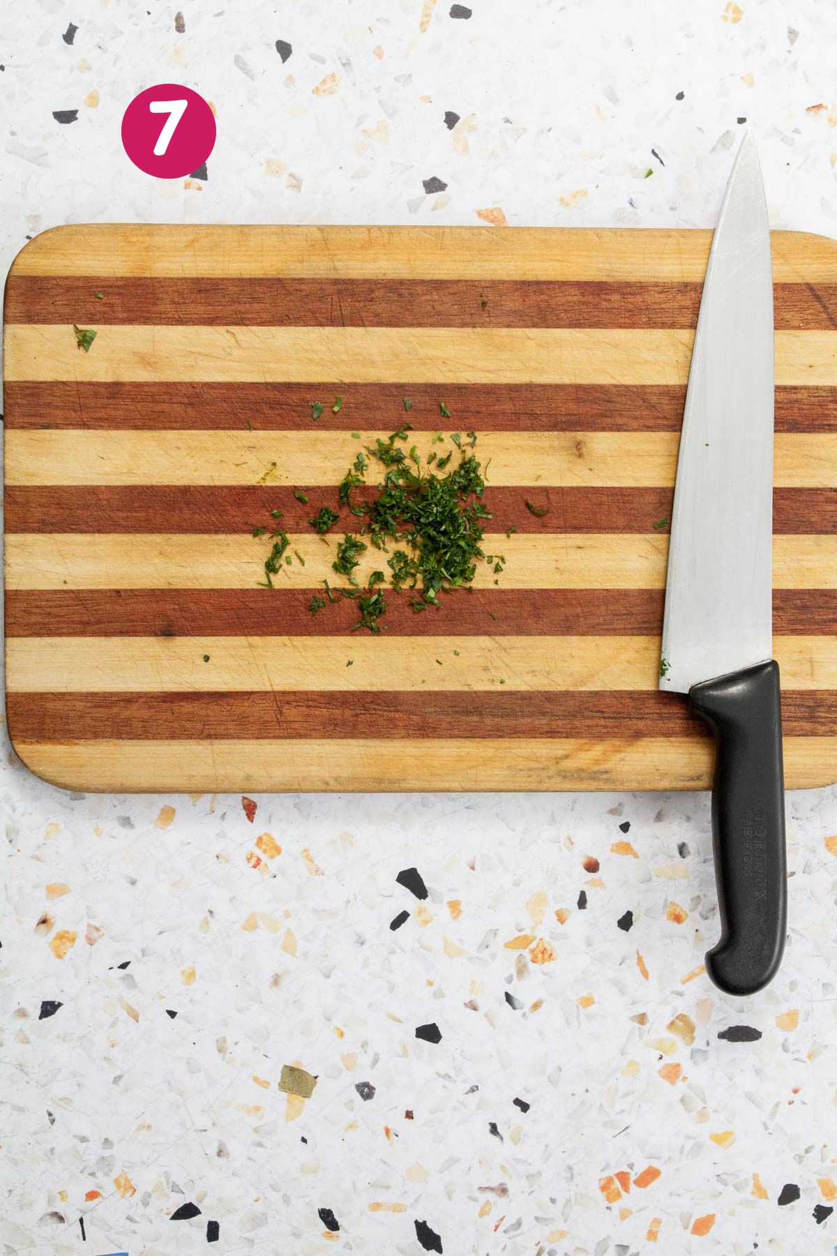 Freshly chopped parsley or cilantro on a striped wooden cutting board with a chef's knife.