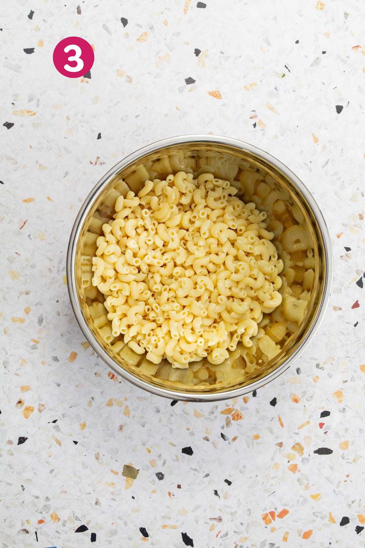 Cooked elbow macaroni pasta in a stainless steel bowl, ready to be assembled into a salad.